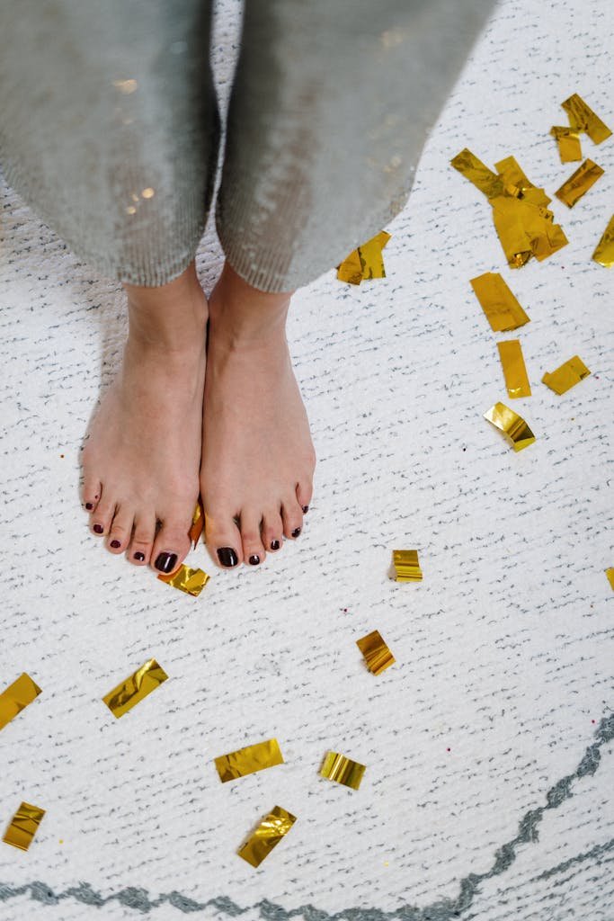 Bare feet on a carpet surrounded by golden confetti, evoking a casual, festive atmosphere indoors.