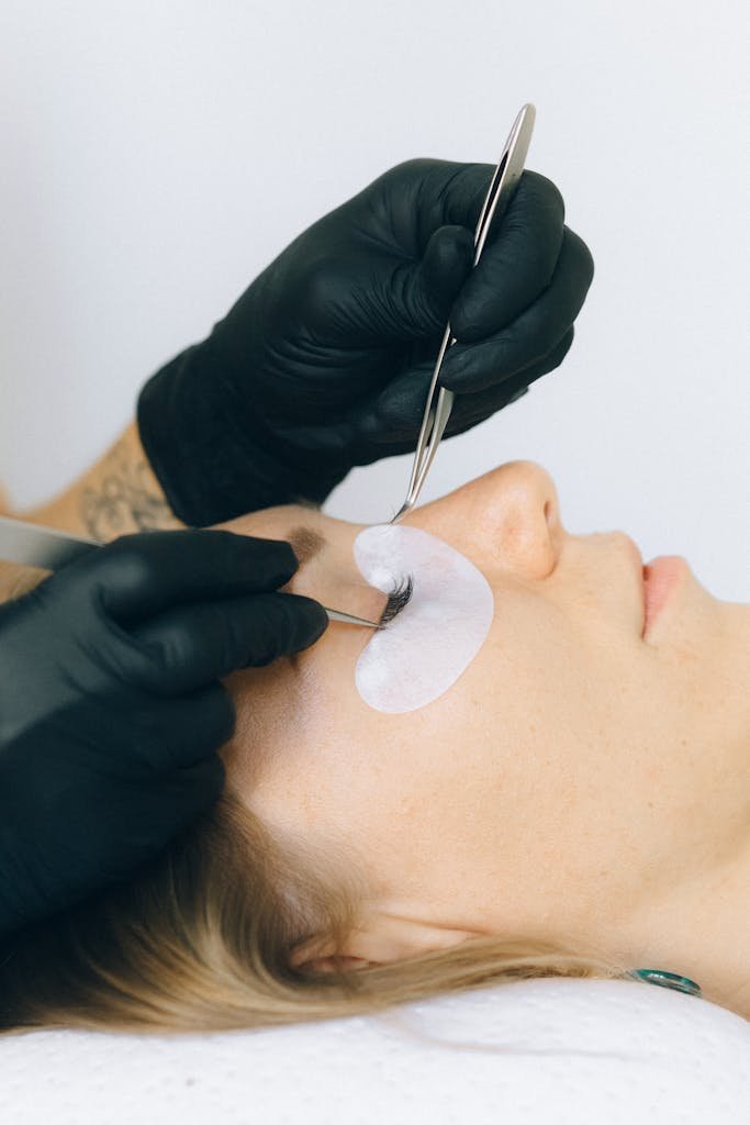 Close-up of a beautician applying eyelash extensions to a client in a salon setting.